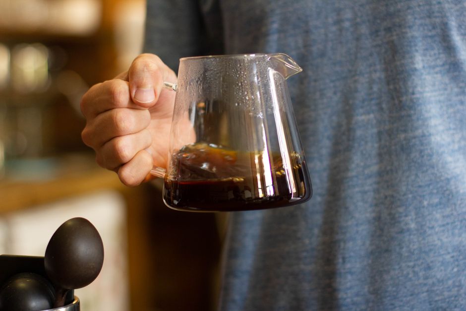 Hand holding a glass coffee server filled with freshly brewed coffee, showcasing rich color and detail.