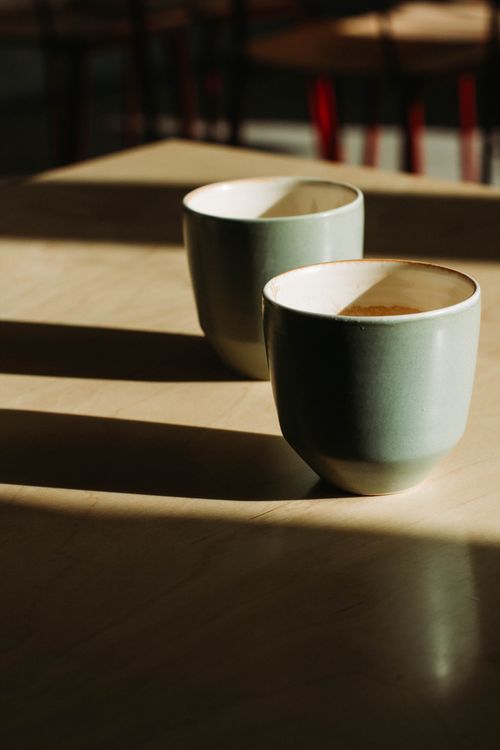 Free Two ceramic cups casting shadows on a sunlit wooden table, highlighting simplicity. Stock Photo