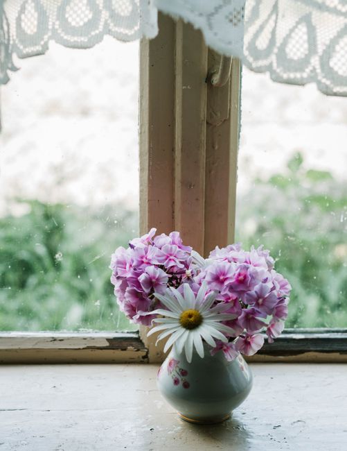 Delicate purple and white flowers in a vase by a textured vintage window.