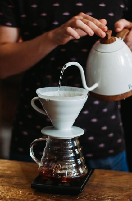Artistic close-up of pour-over coffee brewing with ceramic kettle and filter at home.