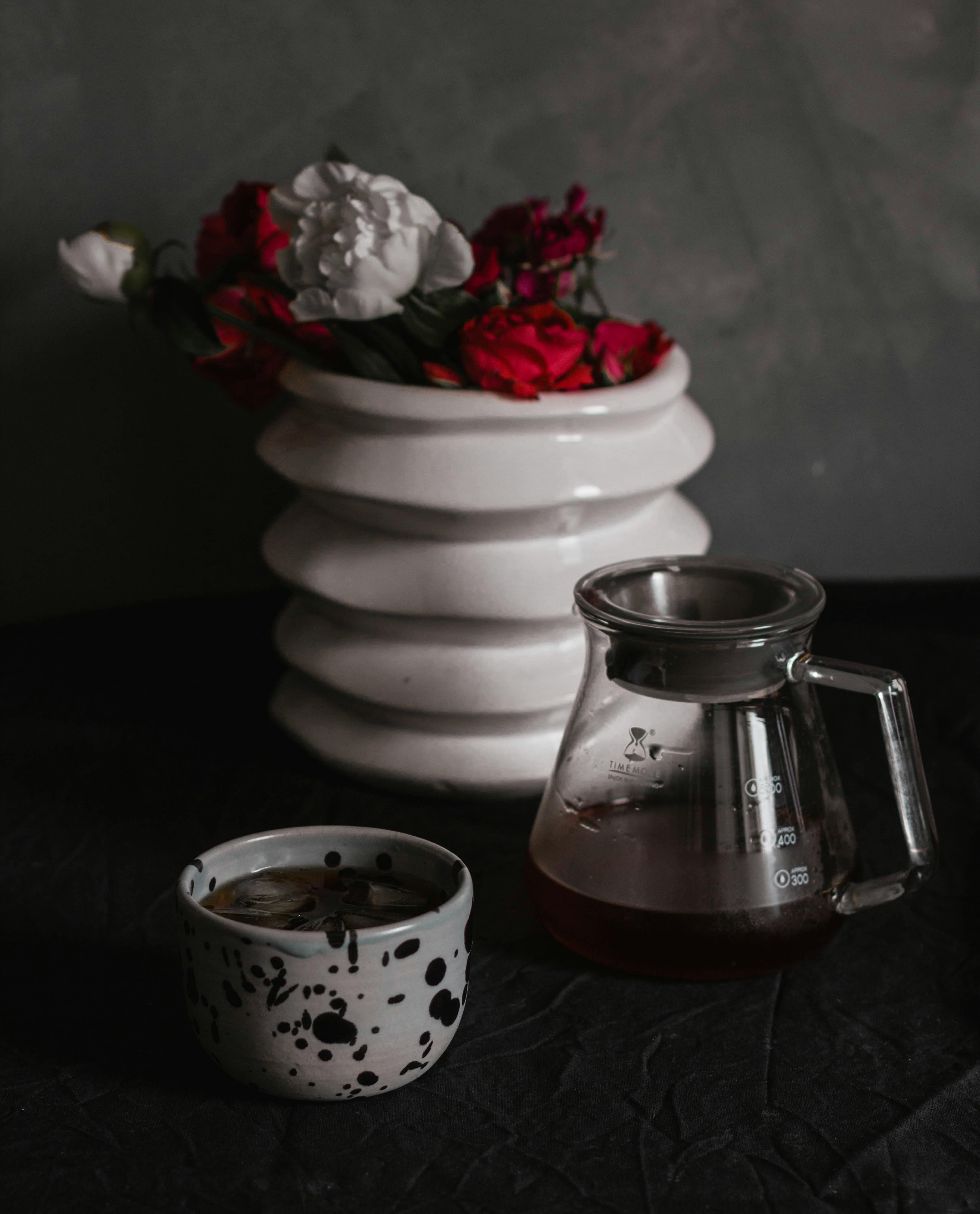 A stylish still life featuring a coffee cup, glass pitcher, and floral vase.