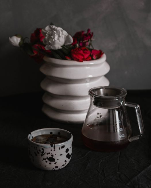 A stylish still life featuring a coffee cup, glass pitcher, and floral vase.