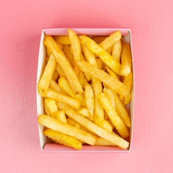 A serving of golden french fries in a box on a vibrant pink surface.