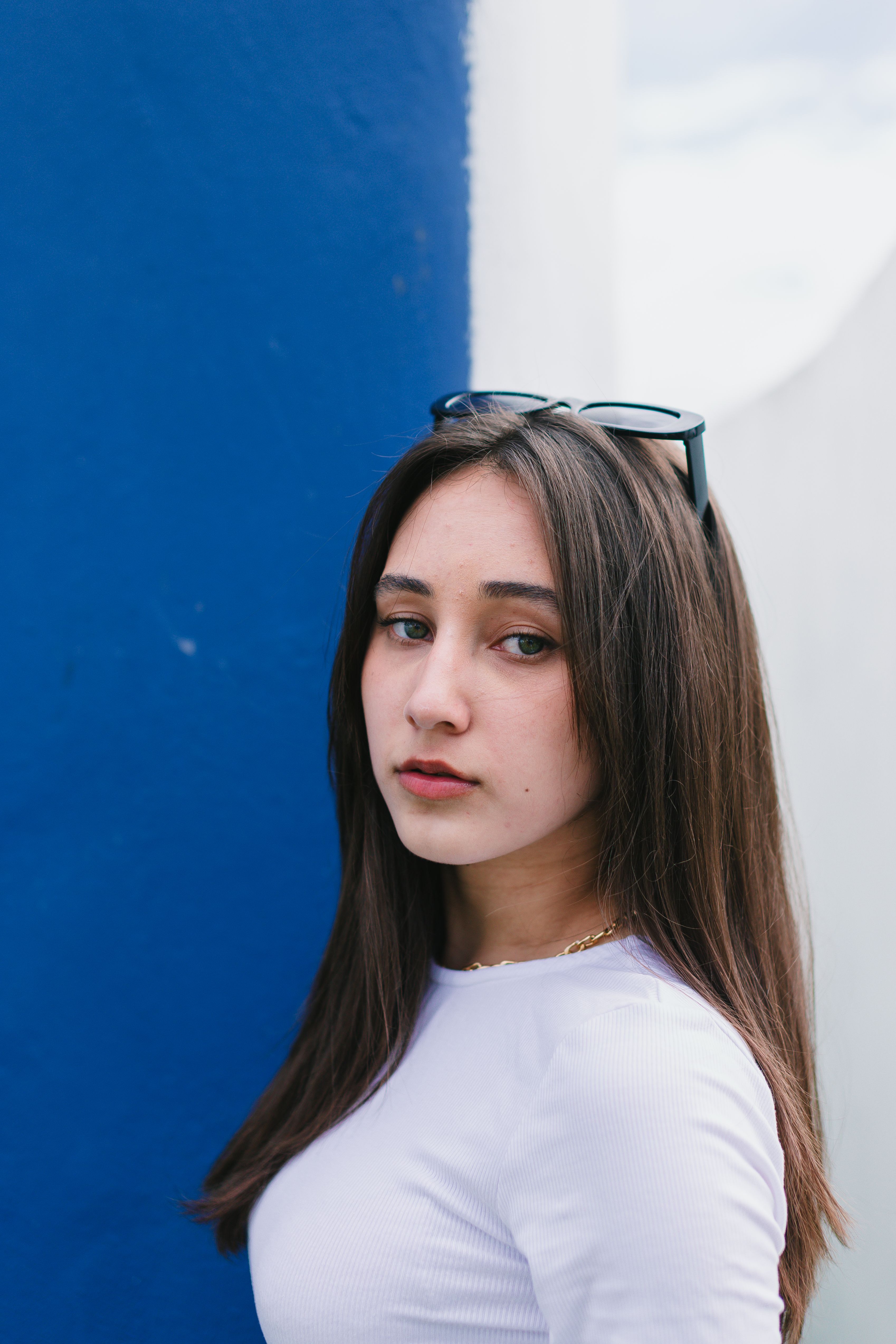 Elegant portrait of a young woman with sunglasses against a blue wall.