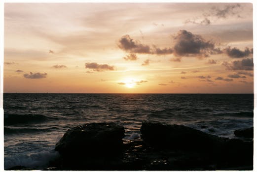 Stunning sunset over the ocean with rocks in the foreground and dramatic clouds.