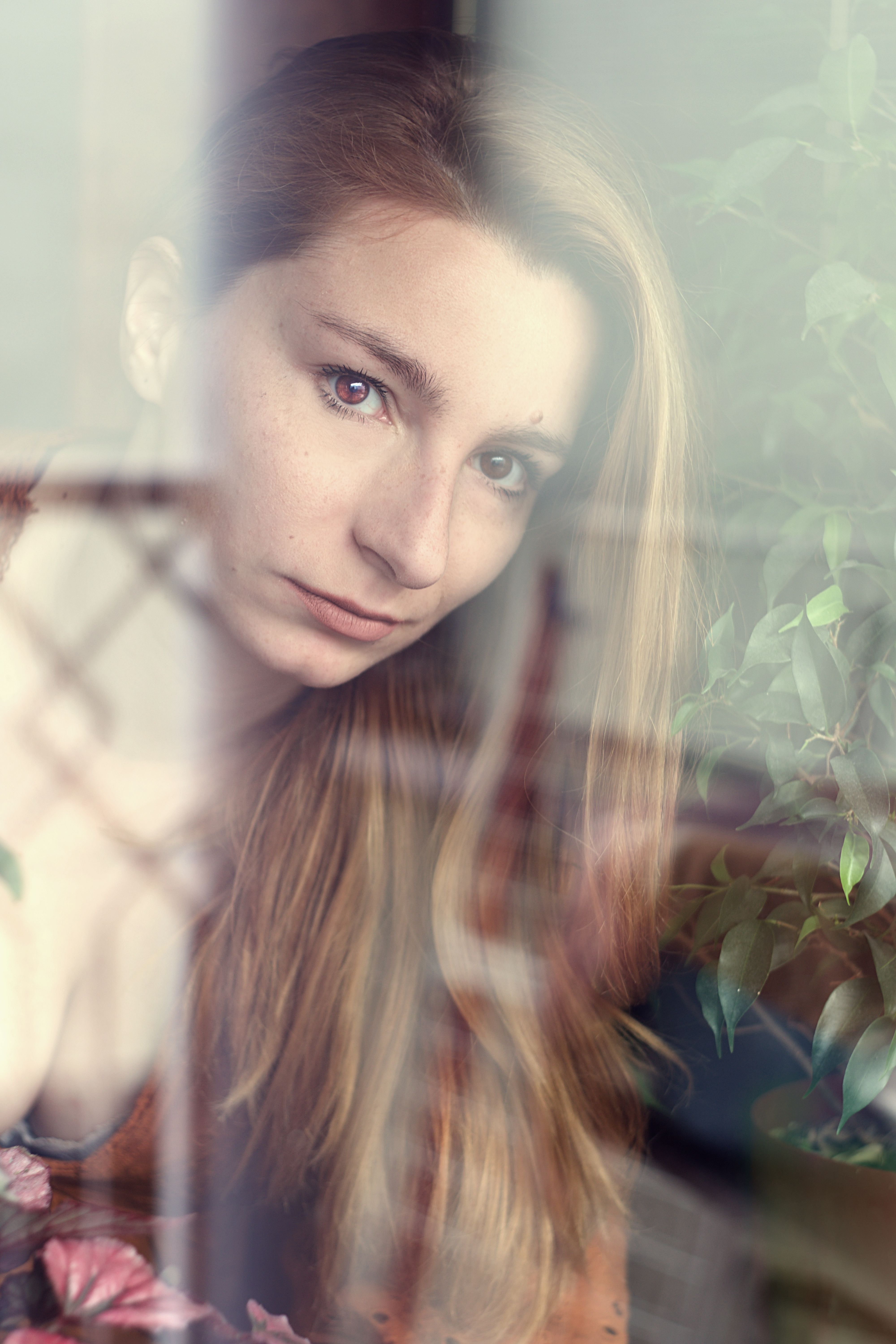 Captivating portrait of a woman gazing through a window, surrounded by plants.