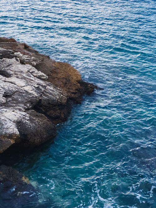 Free Stunning view of a rocky shoreline merging with the crystal-clear blue ocean waves. Stock Photo