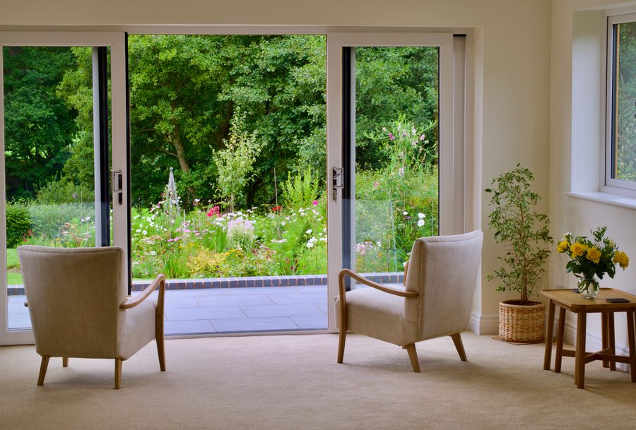 Sunlit living area with two armchairs facing a large sliding glass door open to a green garden