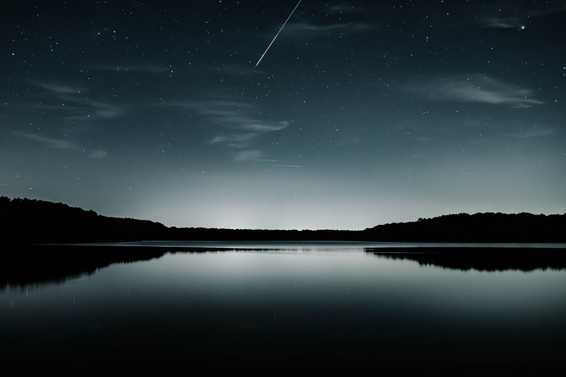 Experience the serene beauty of a starry night with a shooting star over a peaceful lake in Raismes, France.