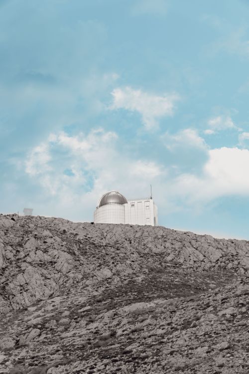 Free A solitary observatory atop a rocky hill set against a vibrant blue sky with clouds. Stock Photo