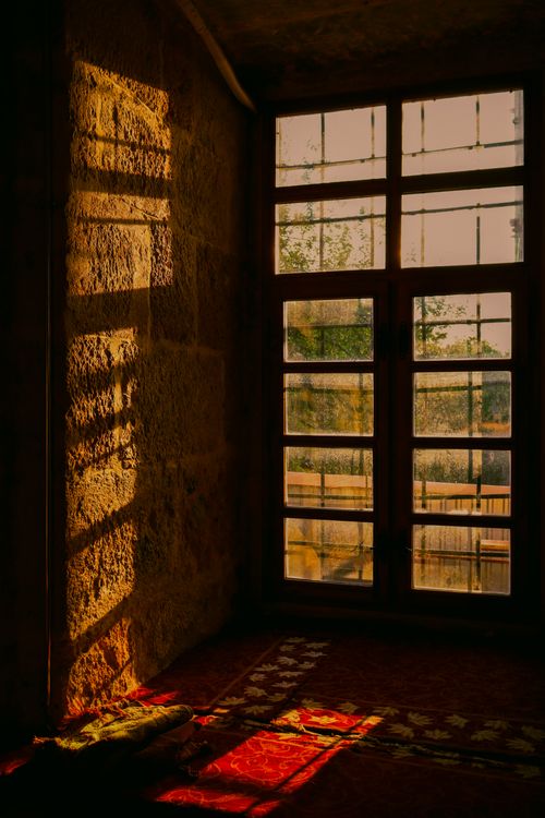 Free Warm sunlight casting shadows in a vintage room with textured walls and wooden windows. Stock Photo