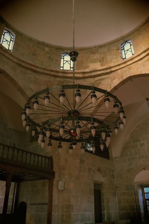 Free A stunning antique chandelier hanging inside a historic stone building with arched windows and ornate design. Stock Photo