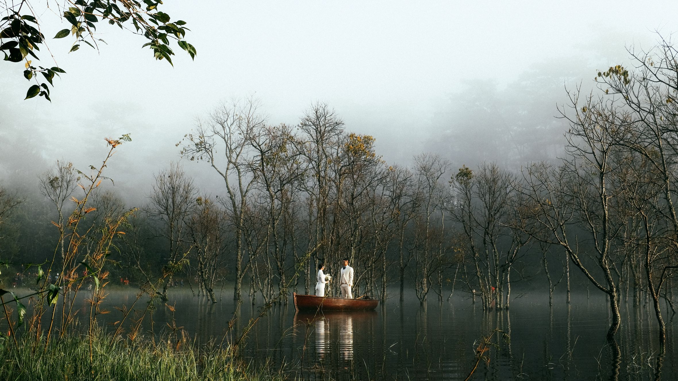 A calm morning scene of a couple in a boat on a misty lake in Dalat, Vietnam.