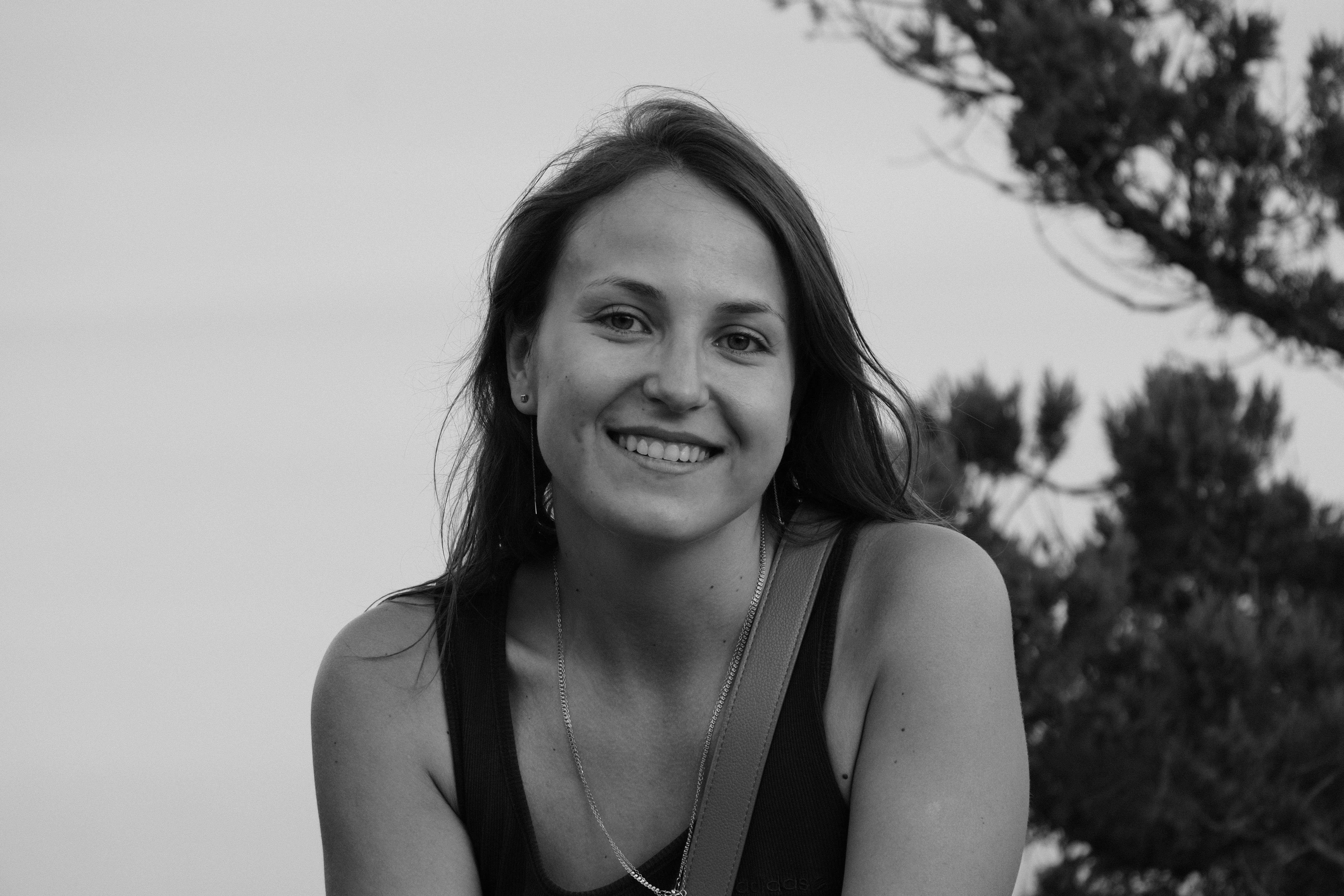 Outdoor black and white portrait of a young smiling woman in a natural setting.