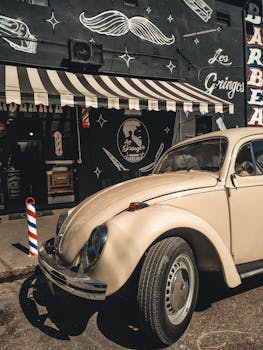 一辆经典米色大众甲壳虫停在一家复古主题理发店前，这家店配有条纹遮阳篷和复古标牌