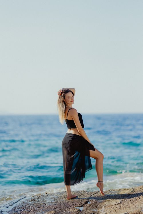 A woman in a black dress is standing on the beach · Free Stock Photo