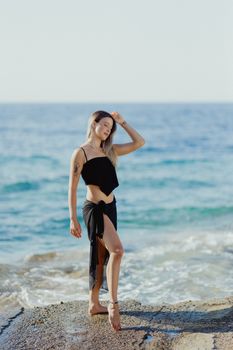 A woman in a black outfit enjoys a sunny day at the beach near the ocean.