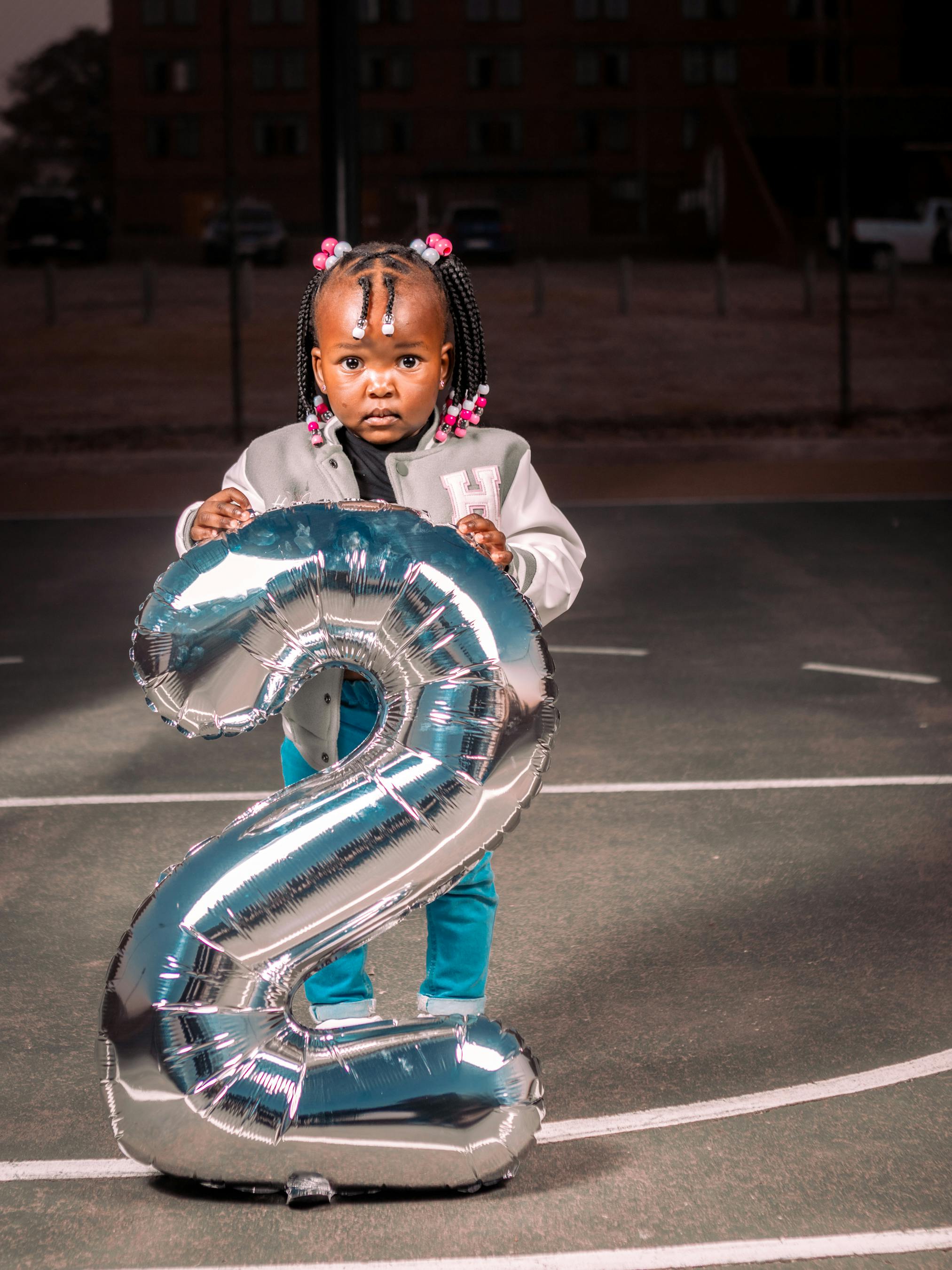 a little girl holding a silver number two balloon