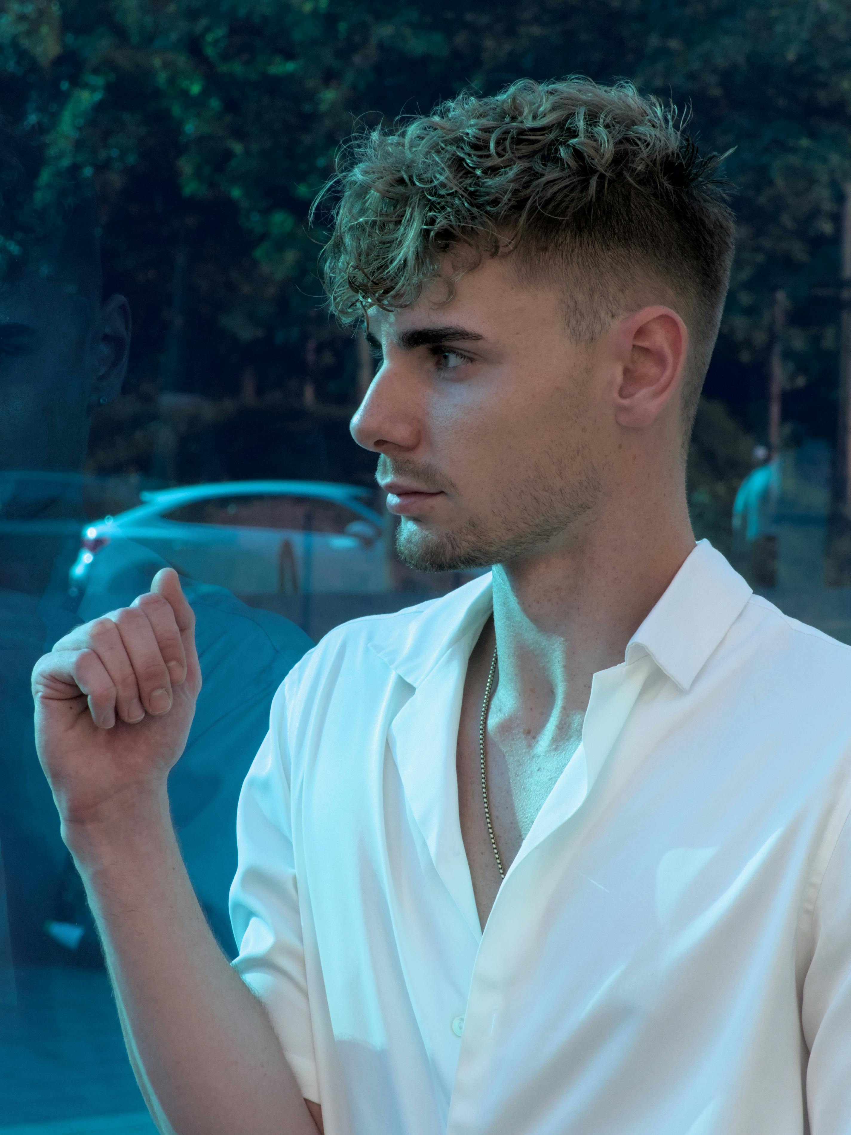 Stylish man standing outside in Berlin, reflecting on a glass surface, wearing a white shirt.