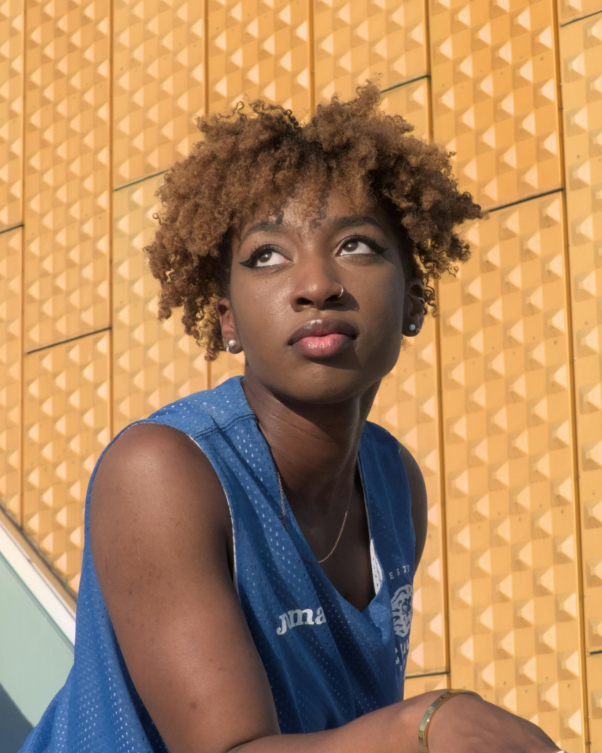 Stylish young woman with afro hair poses outdoors in Berlin, Germany, under the sun.