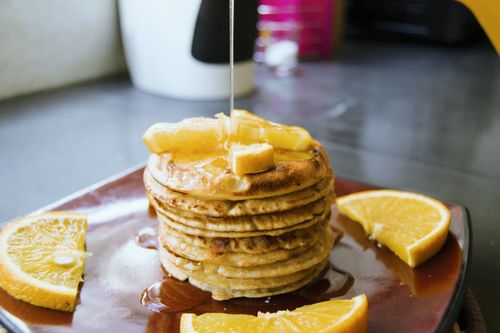Free Tasty homemade pancakes topped with butter and syrup, garnished with fresh orange slices. Stock Photo