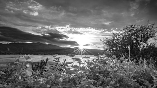 Black and white photo of sun setting over lake