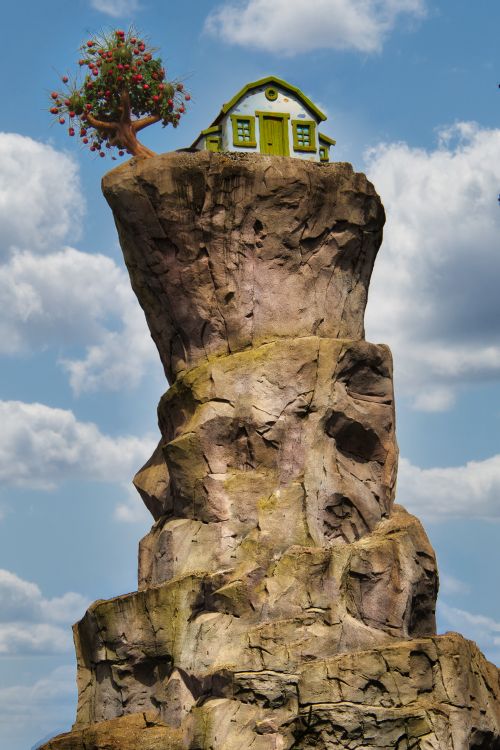 Free A unique house atop a rocky cliff with a tree, under a bright blue sky. Stock Photo