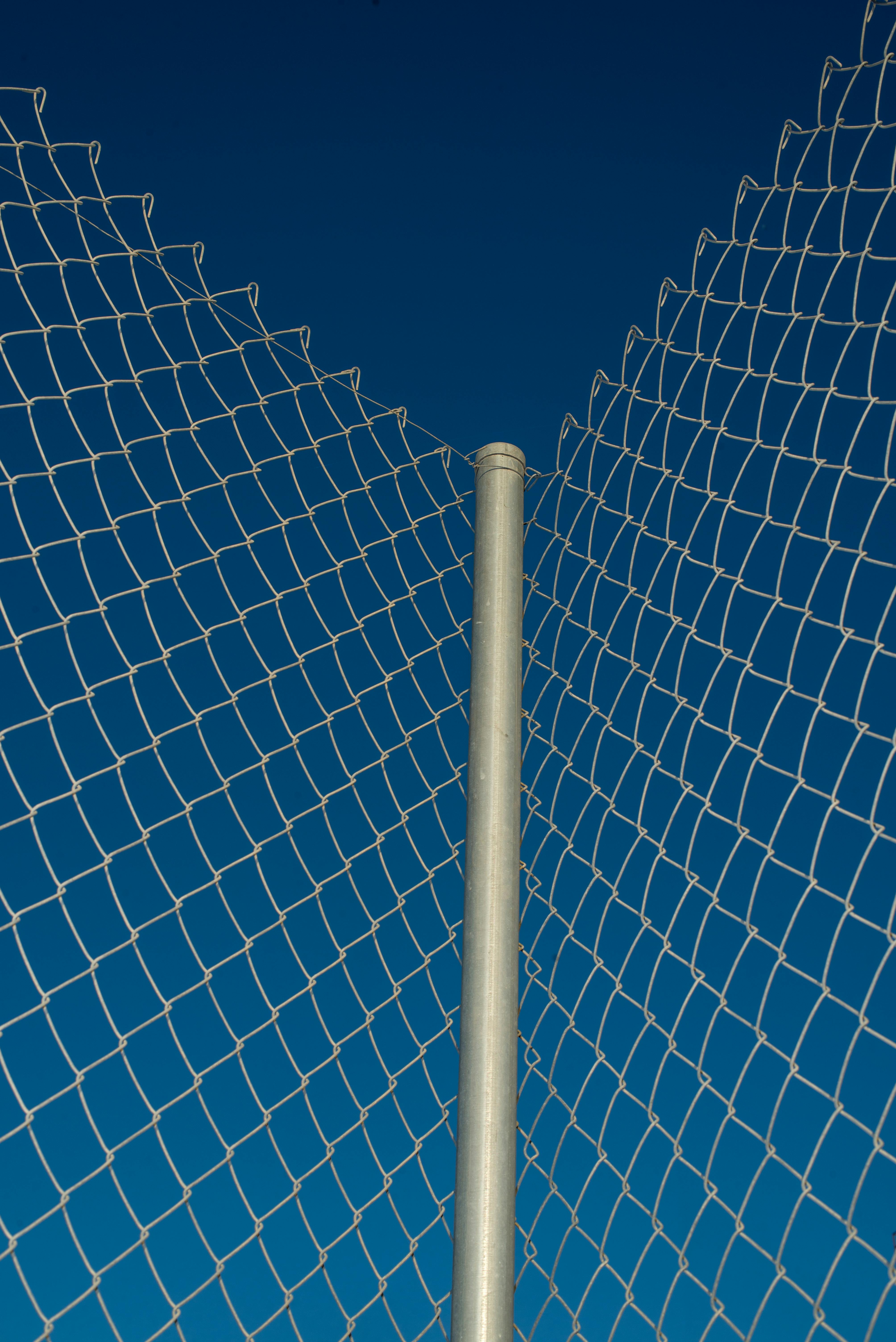Detailed view of a wire mesh fence against a clear blue sky, highlighting geometric patterns.