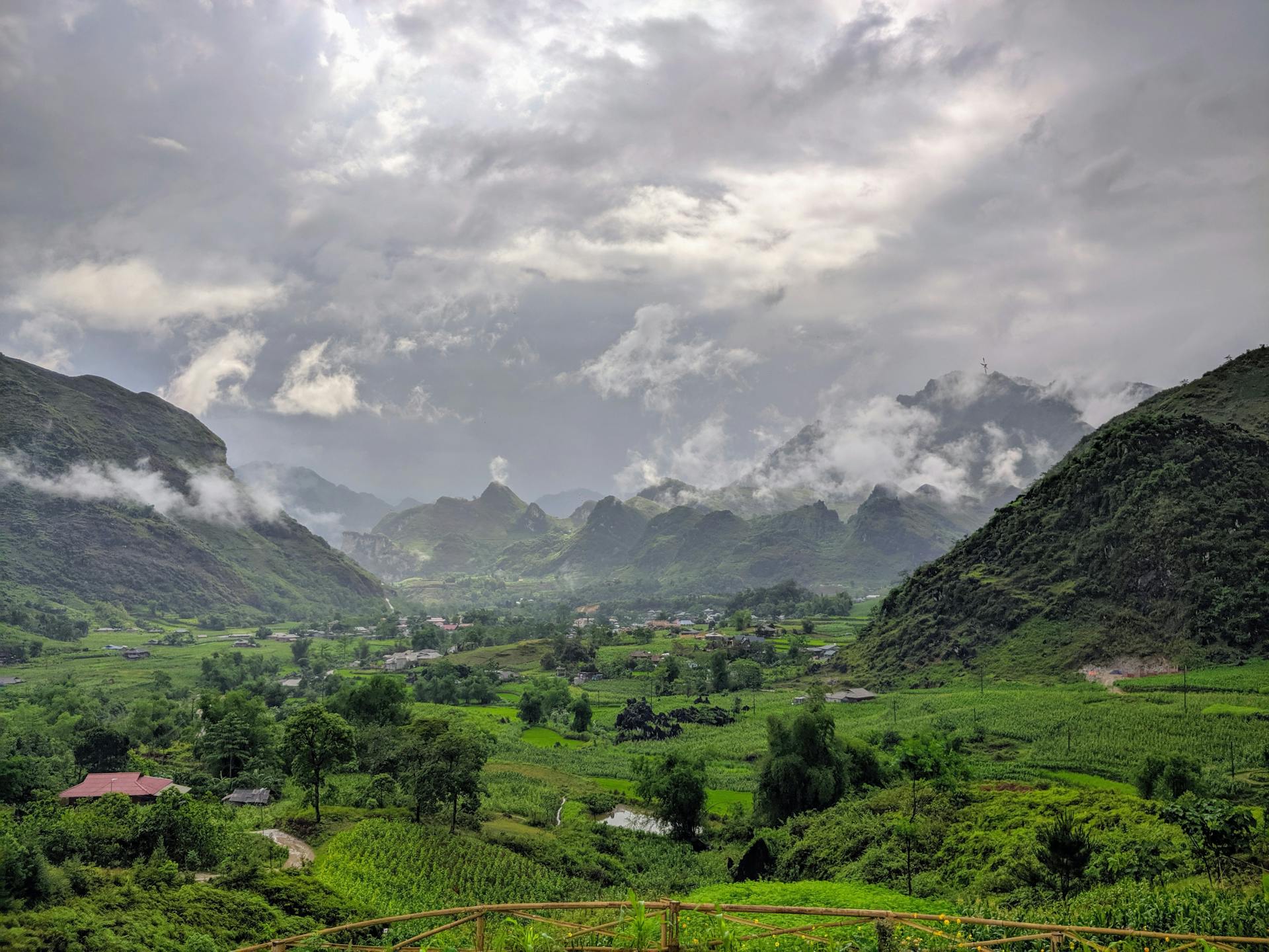 Breathtaking view of Hà Giang's lush green valleys and mist-covered mountains under a dramatic sky.