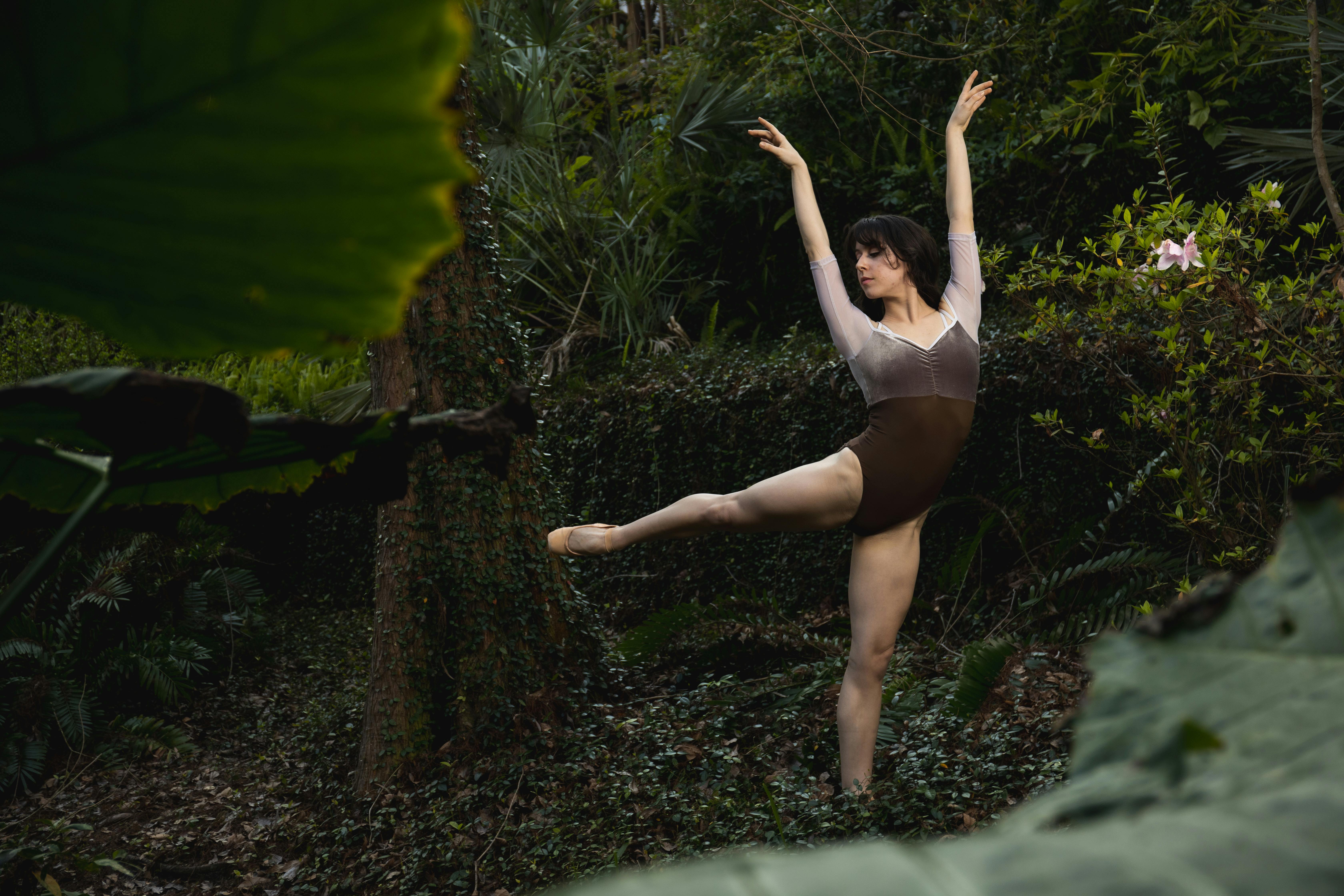 Ballerina in a dance pose surrounded by lush greenery, embodying elegance and nature.