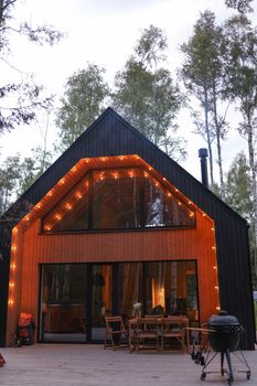A modern cabin with warm string lights in a forest setting, offering a cozy ambiance.