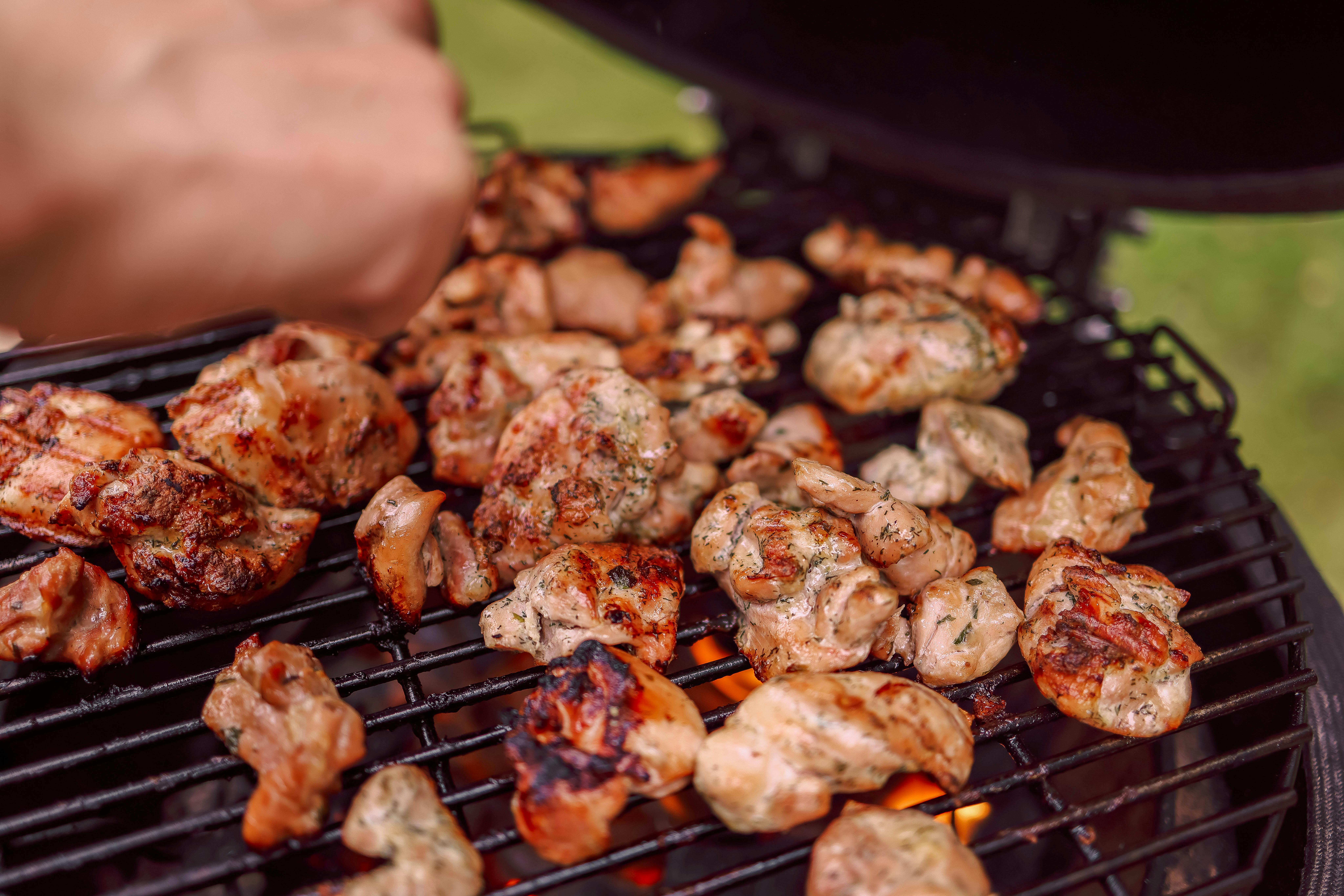 Sizzling chunks of grilled chicken cooking on an outdoor barbecue with charcoal flames.