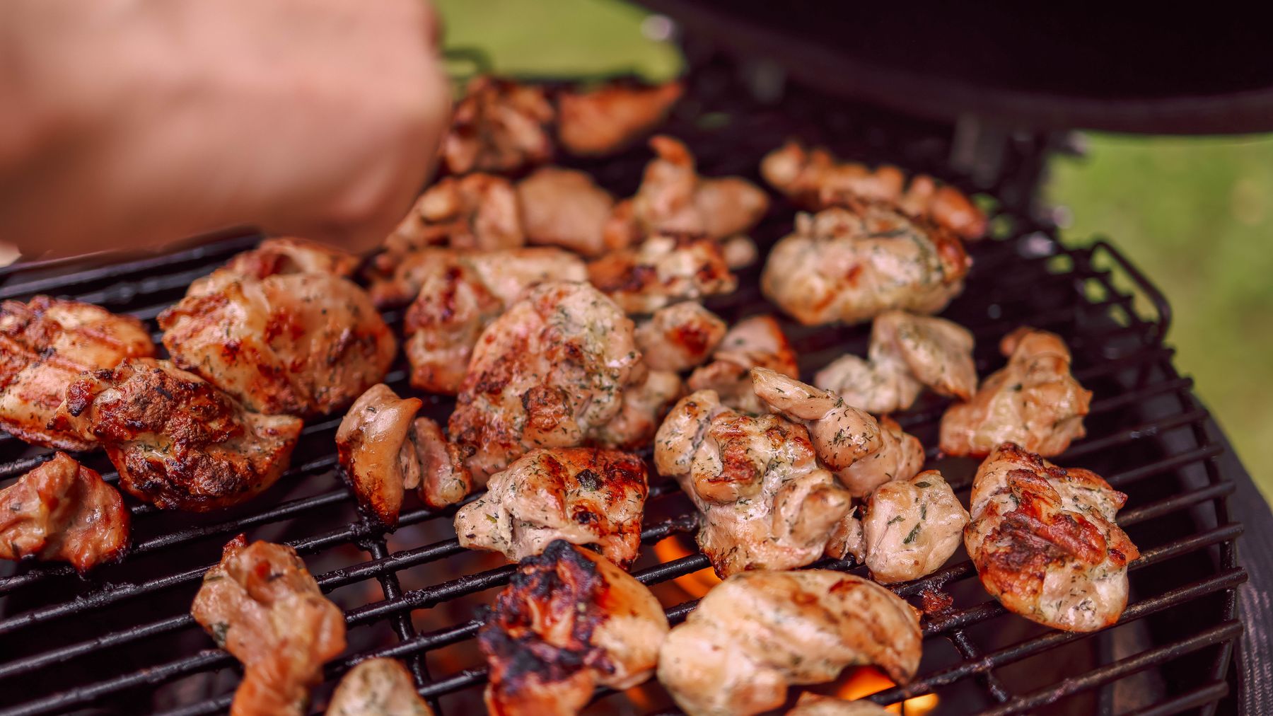 Sizzling chunks of grilled chicken cooking on an outdoor barbecue with charcoal flames.