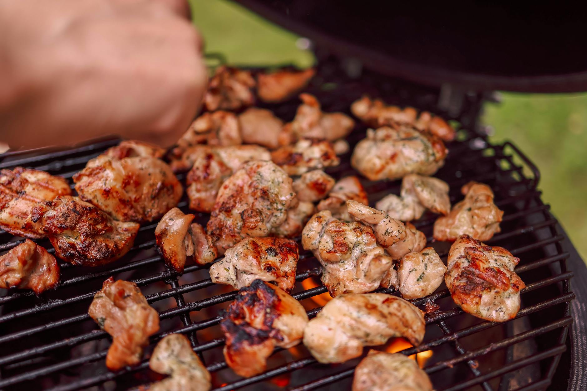 Sizzling chunks of grilled chicken cooking on an outdoor barbecue with charcoal flames.