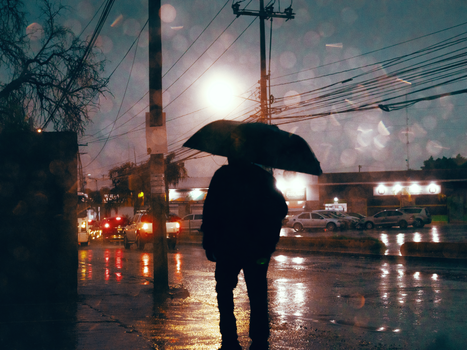 Silhouette of a person with an umbrella on a rainy evening street in Querétaro, Mexico.