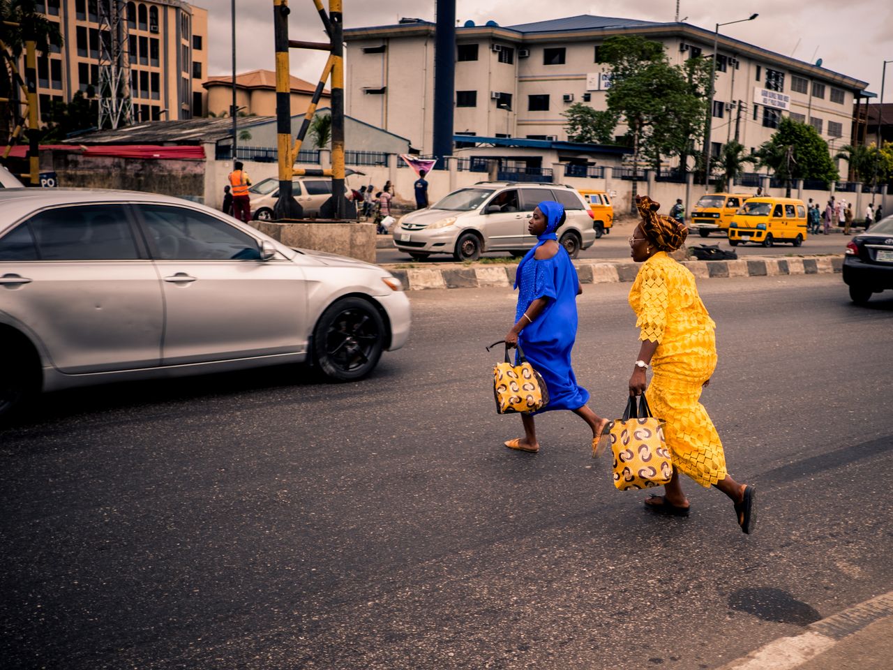 two women in traditional nigerian outfits cross a bustling street in l