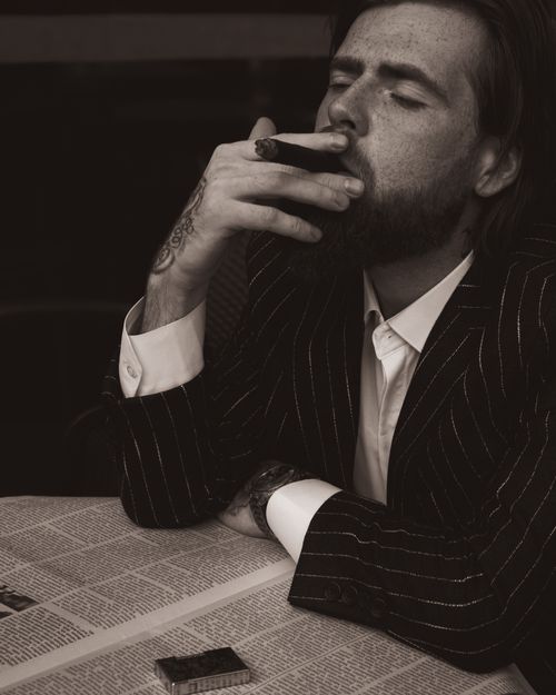 Free A stylish man in a pinstripe suit smokes a cigar thoughtfully indoors. Stock Photo