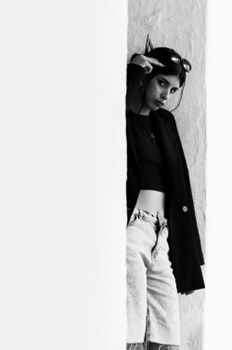 Black and white portrait of a fashionable young woman leaning against a wall.