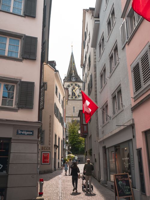 Free Picturesque view of a Zurich street featuring St. Peter's Church and the Swiss flag. Stock Photo