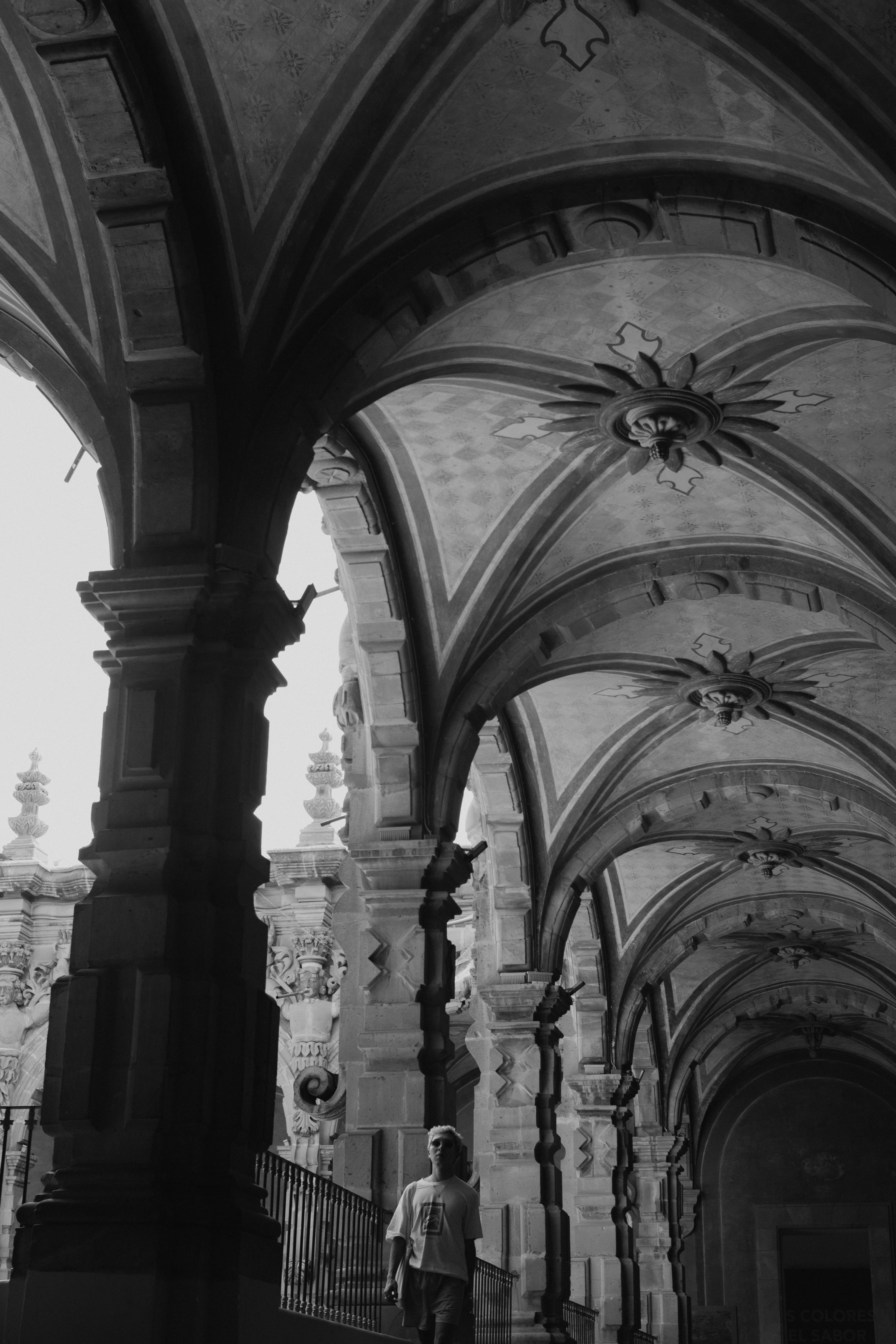 a black and white photo of a man walking under a arch