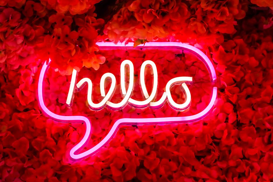 A bright pink neon 'Hello' sign illuminating a luxurious red floral background, perfect for pop art designs.