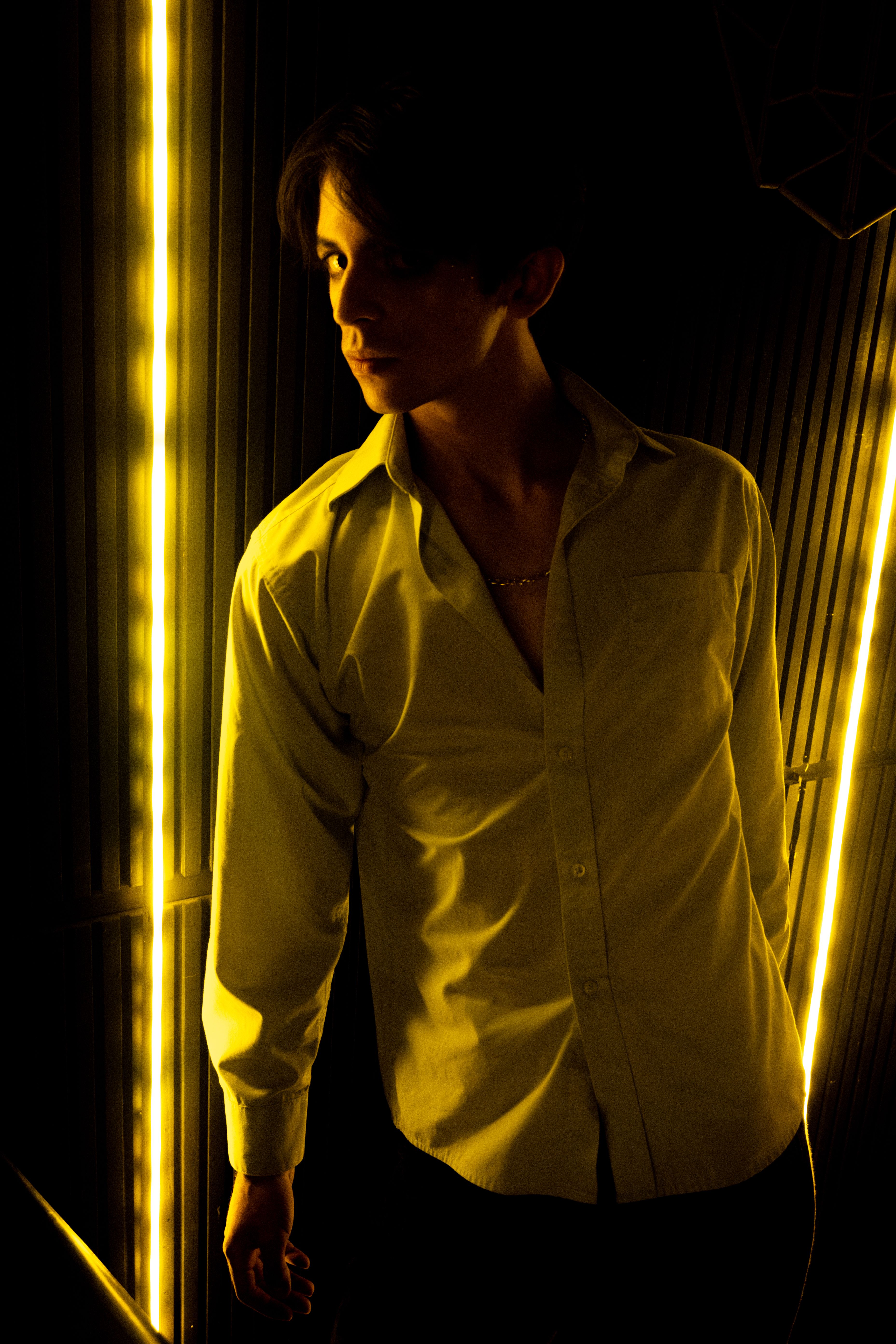 A man poses in dramatic lighting, highlighting fashion and shadows in an artistic portrait.