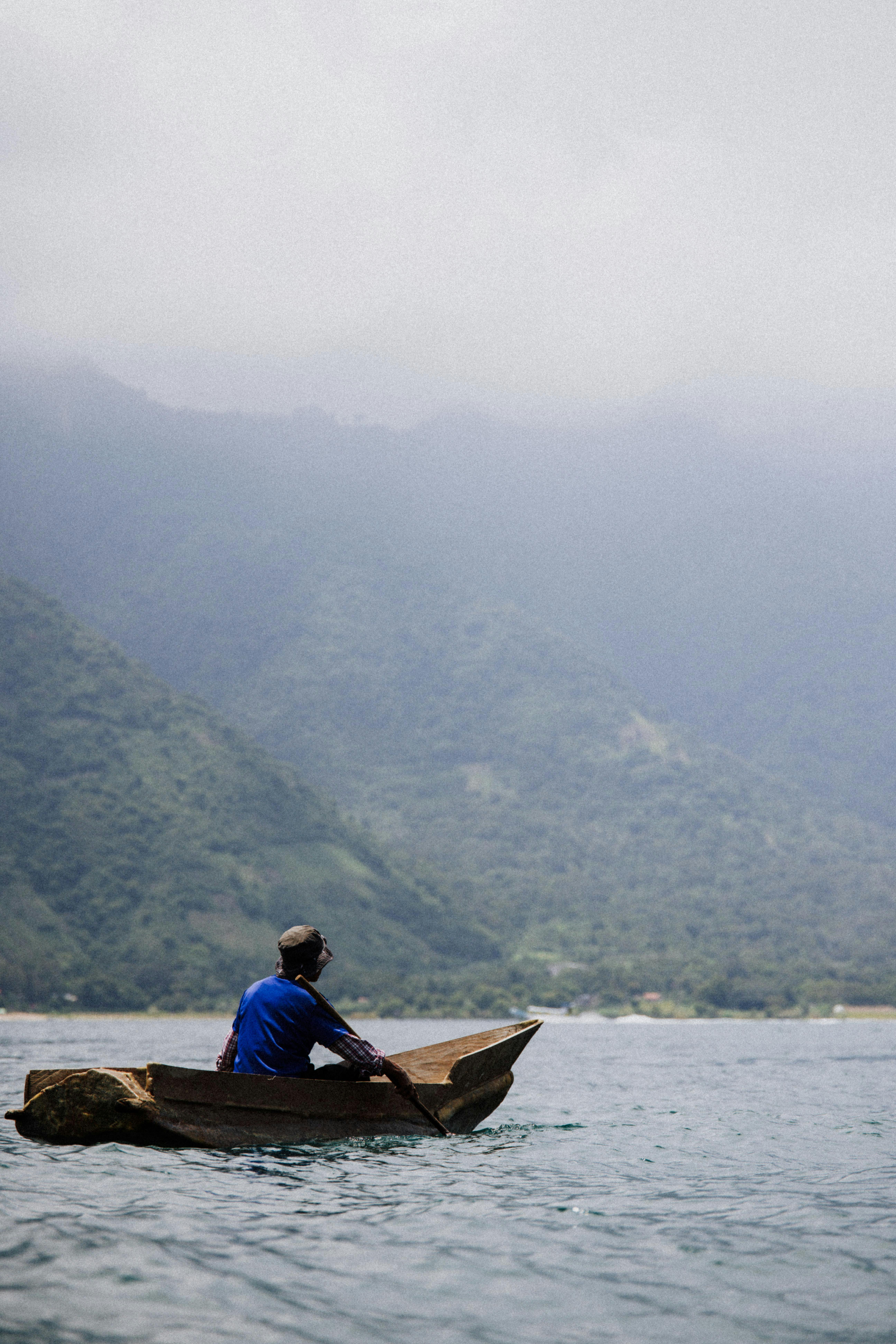 A solitary fisherman paddling a wooden canoe on a misty lake with mountain backdrop.