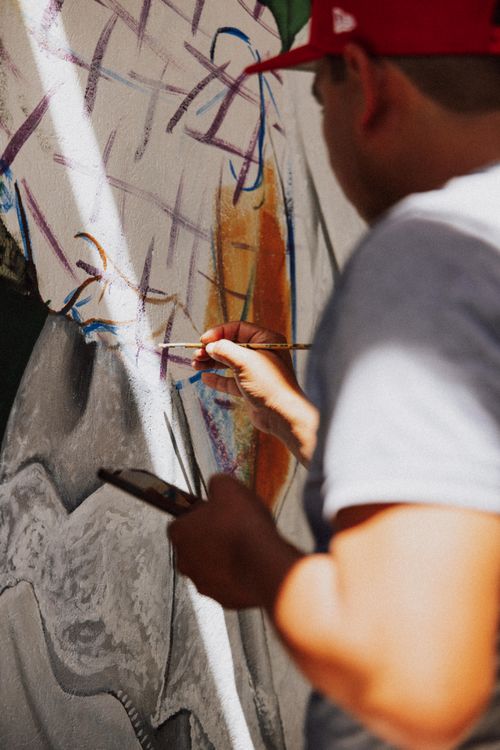 Free A focused street artist painting a colorful mural on an outdoor wall, showcasing urban creativity. Stock Photo
