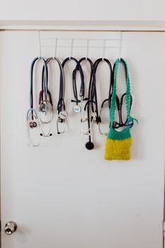 Multiple stethoscopes hang on door hooks, showcasing a medical setting.