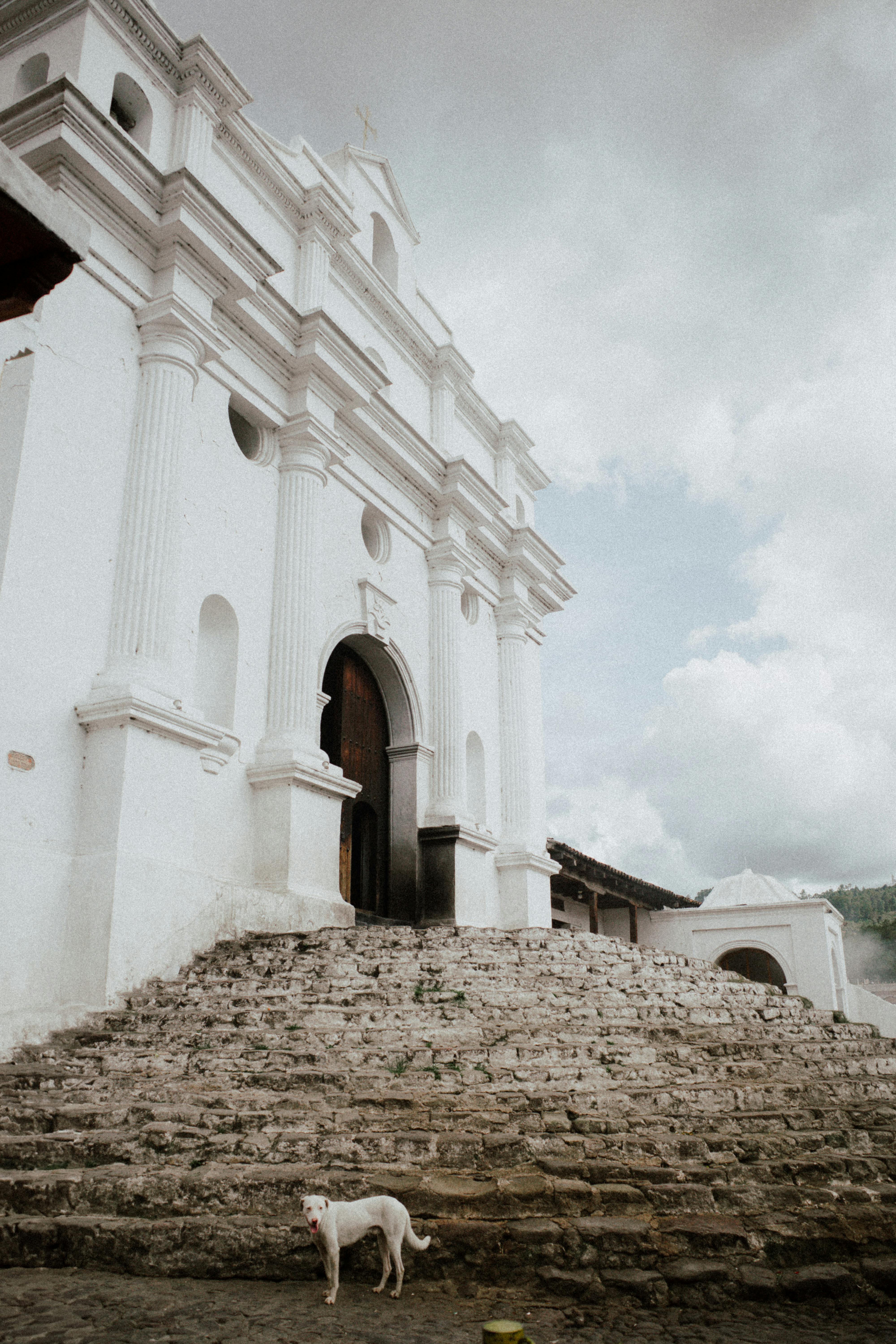 Old white church with arched entrance and stone steps, located outdoors on a cloudy day.