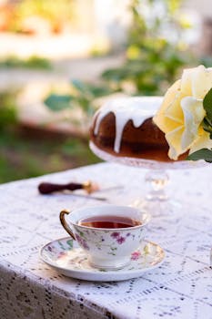 A charming outdoor tea setup with a floral teacup and cake on lace tablecloth, perfect for afternoon relaxation.