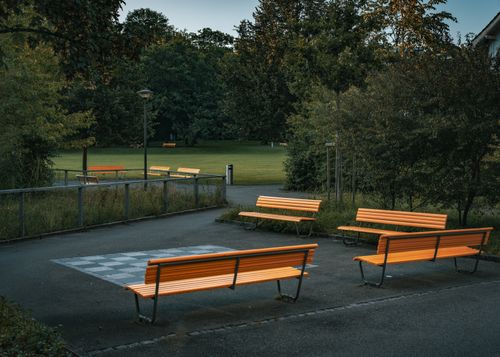 Free Tranquil view of orange benches in an empty park surrounded by lush autumn trees. Stock Photo