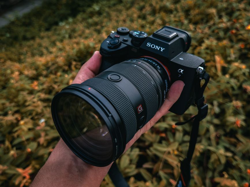 Fotógrafo segurando câmera mirrorless com objetiva teleobjetiva em ambiente externo com luz natural