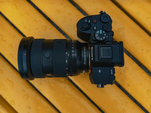 Free Top view of a digital camera with lens resting on a yellow wet surface, showing its controls and design. Stock Photo